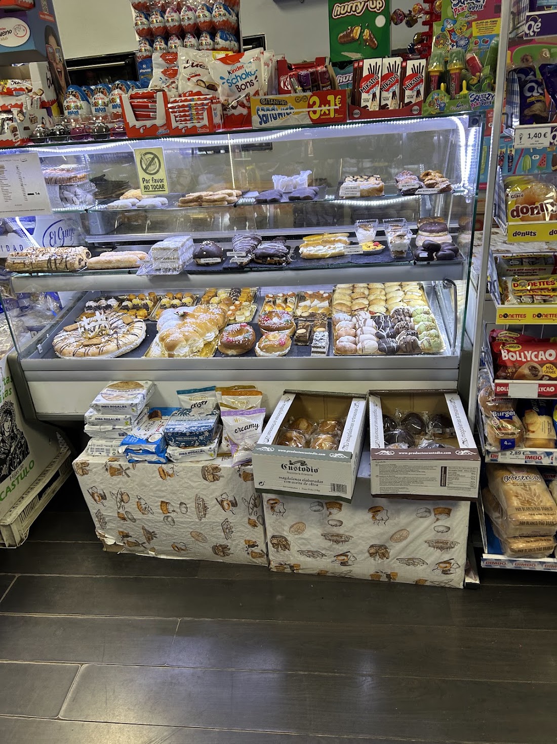 Vitrina con dulces y bollería junto a estanterías de alimentación